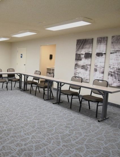 A conference room with a U-shaped setup of gray tables and chairs, light carpet, framed photos on the walls, and a doorway at the back.