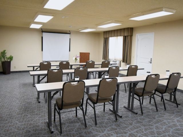A small conference room set up with rows of tables and chairs facing a projector screen and podium, ready for a meeting or training session.