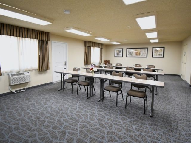 A small classroom or meeting room with two long tables and several chairs, framed pictures on the wall, windows with curtains, and a patterned carpet, all arranged for a seminar.