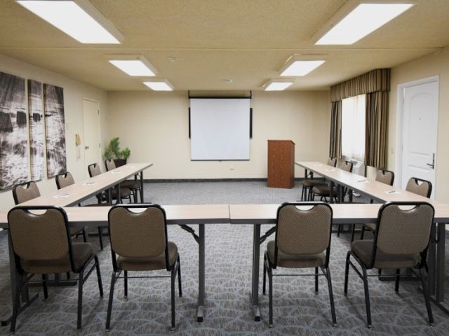 A conference room setup with folding chairs arranged in a U-shape around a central projector screen and podium, ready for a meeting.