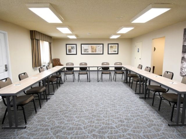 A conference room set up in a U-shape with long tables and chairs, neutral walls, framed art, and soft overhead lighting, ready for a meeting.