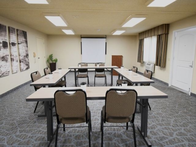 A small conference room set up with U-shaped desks, office chairs, a projector screen, and a podium at the front.