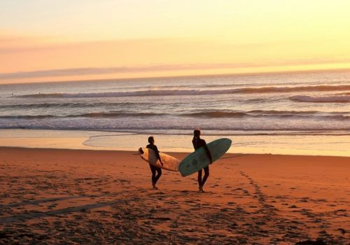 Two surfers walk toward the water with their boards at sunset on the beach.