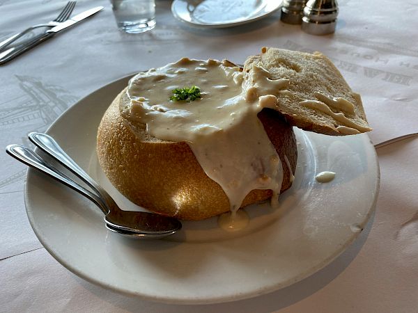 A rustic plate with a puffed English muffin topped by creamy sauce and a sprinkle of parsley, plus a small slice of toasted bread on the side.