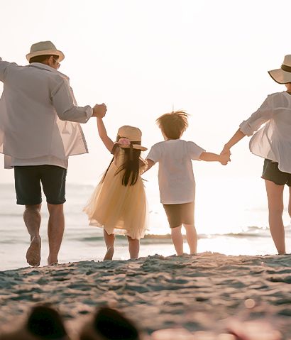 A family holds hands and walks along the beach at sunset, celebrating togetherness and joy as waves meet the shore.