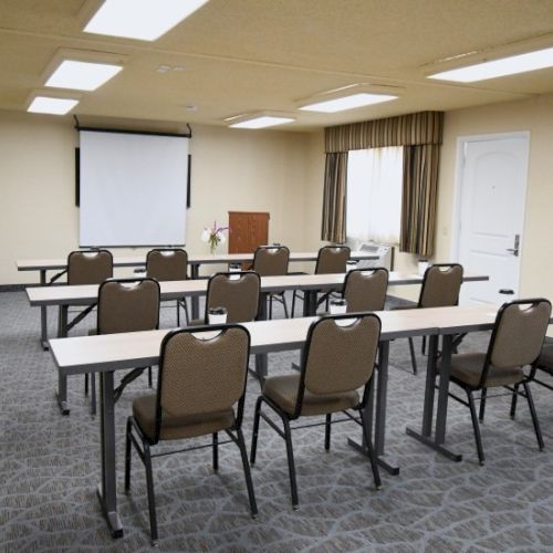 A small conference room set up for a presentation, with rows of desks and chairs facing a projection screen at the front.