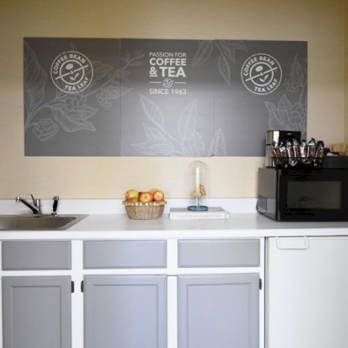 A small coffee nook with a sink, counter space, a toaster/coffee maker, a basket of fruit, and a chalkboard-style sign above.