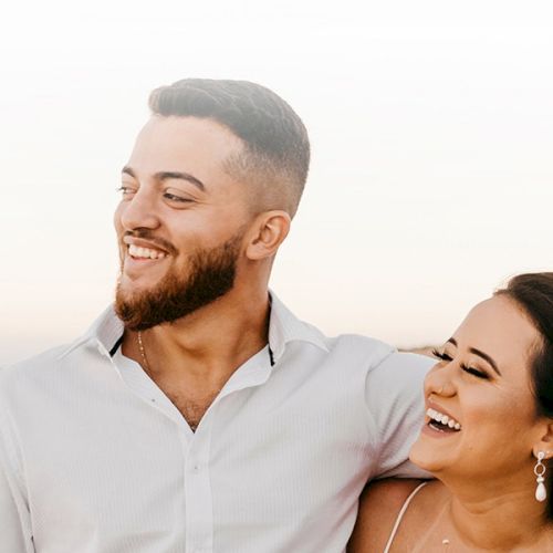 A joyful couple walking along a sunny beach, smiling and holding each other, enjoying a carefree moment by the waves.